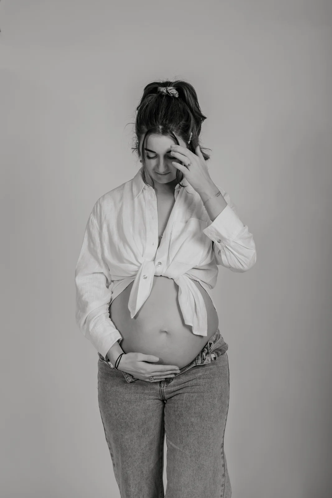Zwart-witportret van een aanstaande moeder in witte blouse, hand in het haar